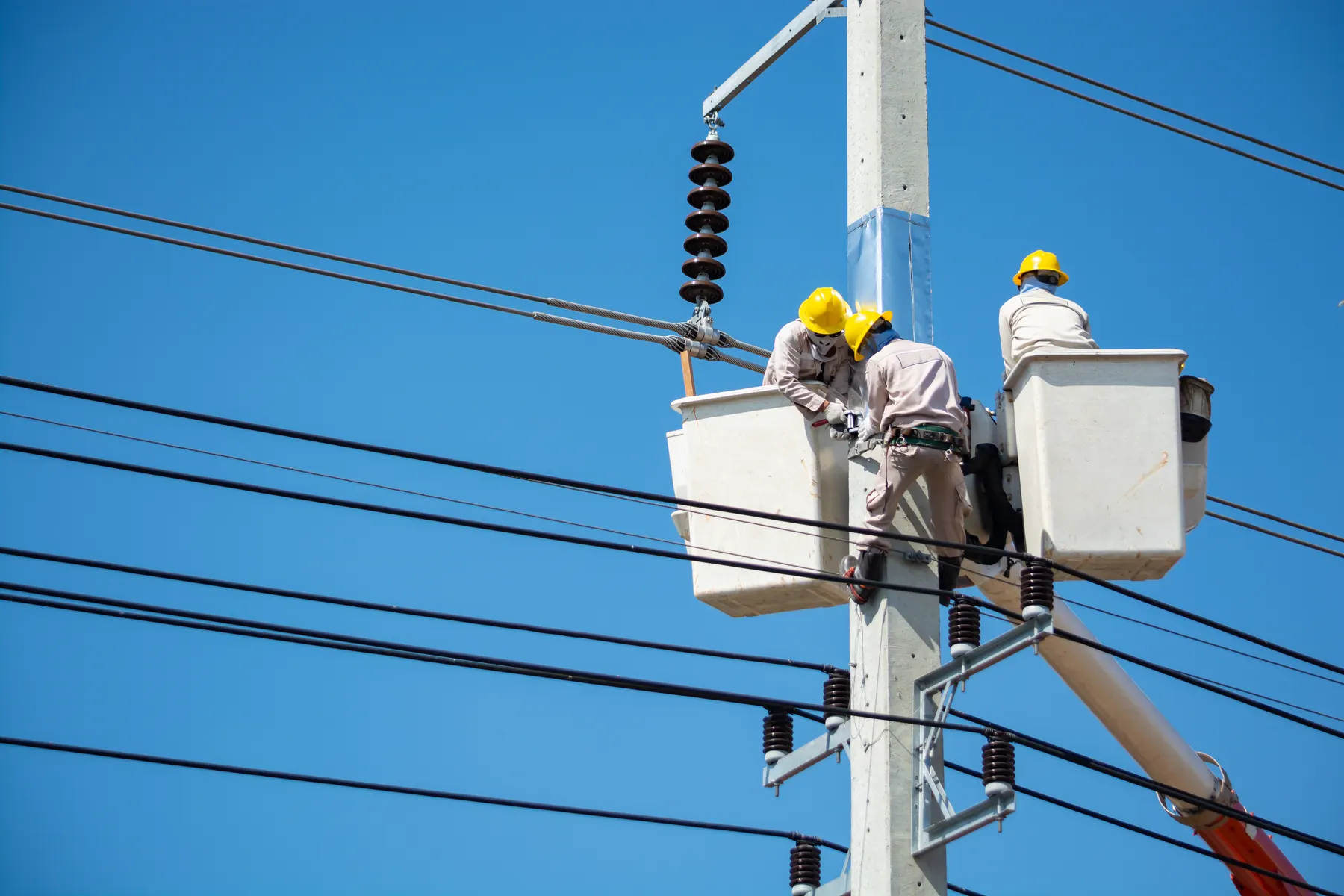 Line crew working from a bucket truck against a blue sky
